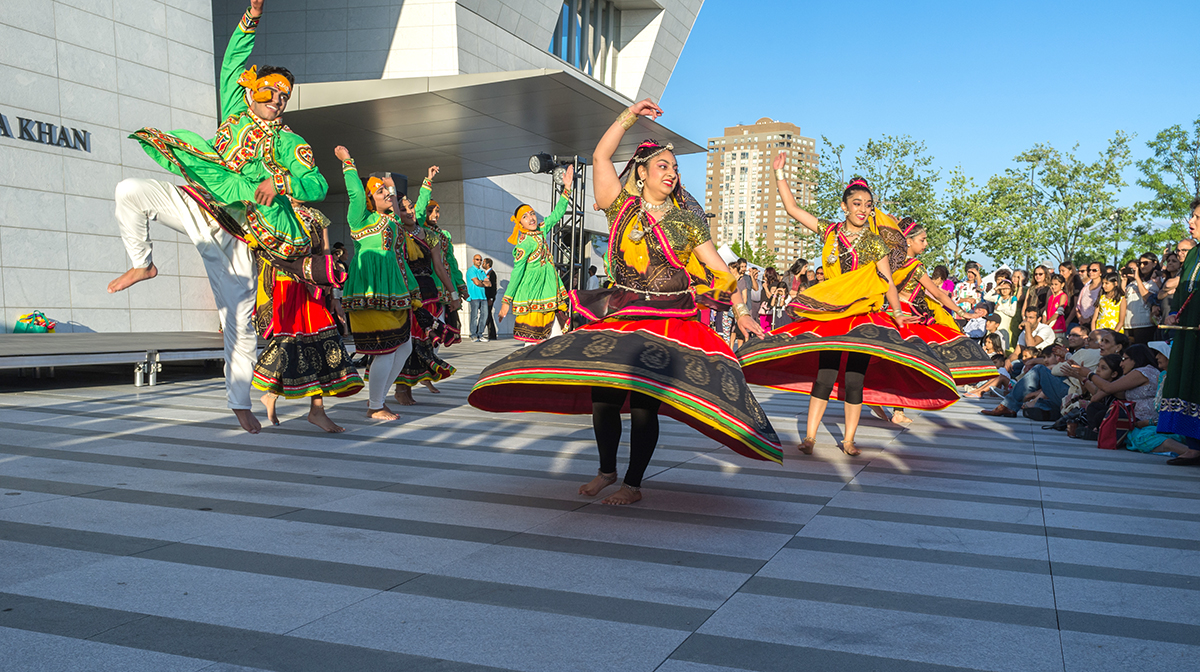 A group of large colourfully dressed dancers performing in front of the Museum.